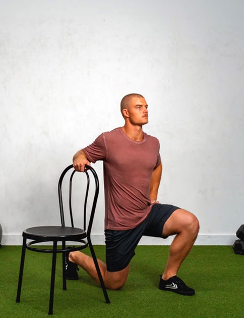 man doing a lunge holding a chair for support stock image