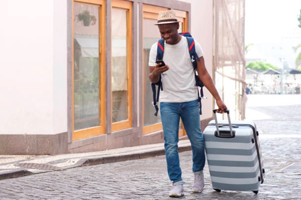 man pulling suitcase along a street and checking phone stock image