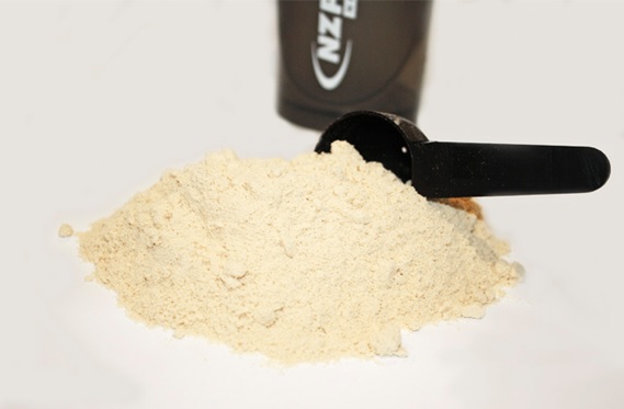 pile of protein powder on table with scoop and shaker in background