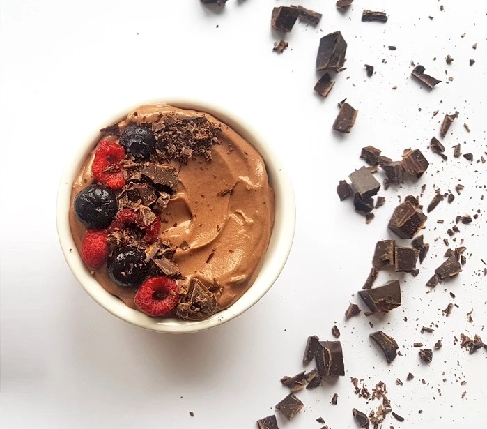 white bowl of chocolate mousse with chocolate around it and berries