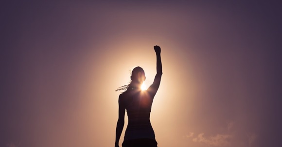 woman standing in front of sun rise with raised arm