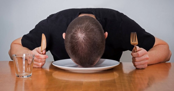 person at dinner table clutching knife and fork with their head on empty plate stock image
