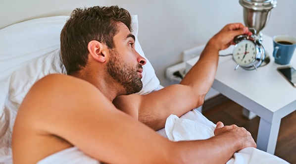 man lying in bed checking a large clock stock image