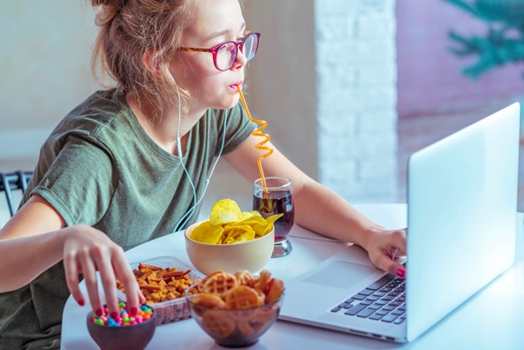 woman sitting at laptop eating snack foods stock image