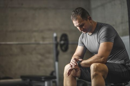 man in the gym between exercise looking at fitness watch stock image