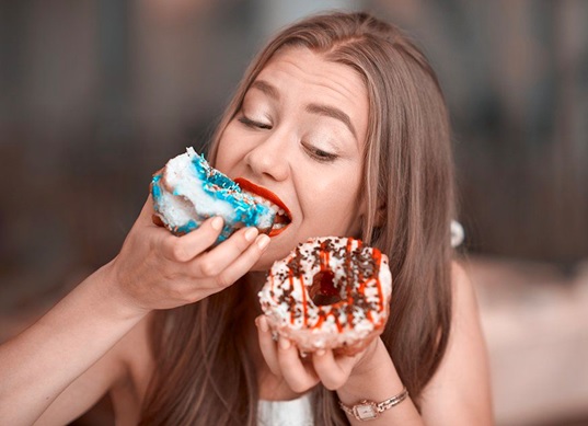 woman holding donuts in both hands eating one stock image